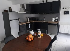 A modern kitchen with dark cabinetry, a built-in oven, and a dining table set with fruits and a teapot.