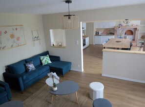 Una sala moderna con un sofá azul, una mesita redonda y una cocina al fondo.