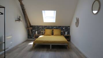 Une chambre avec un plafond en pente, un puits de lumière, un lit avec une literie jaune, une tête de lit en bois et un miroir fixé au mur.