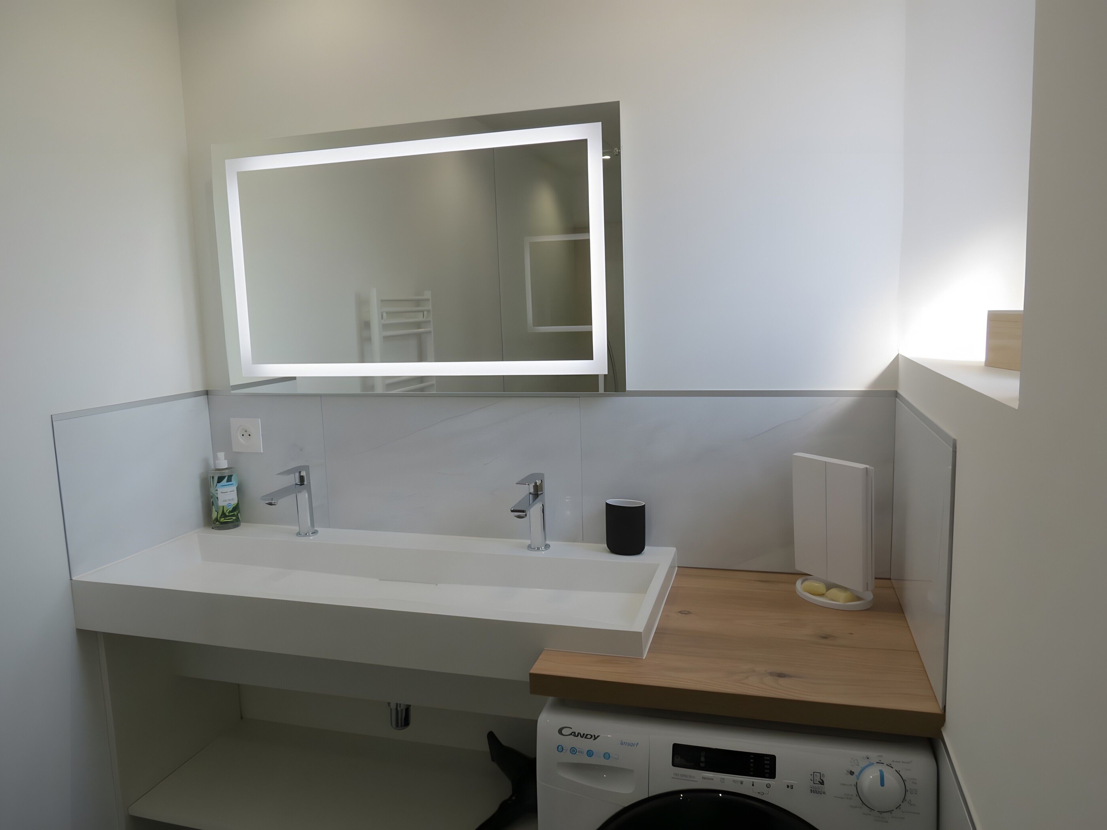 A modern bathroom with a large mirror, a sink, a toilet, and a washing machine.