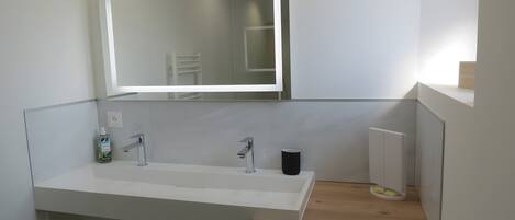 A modern bathroom with a large mirror, a sink, a toilet, and a washing machine.