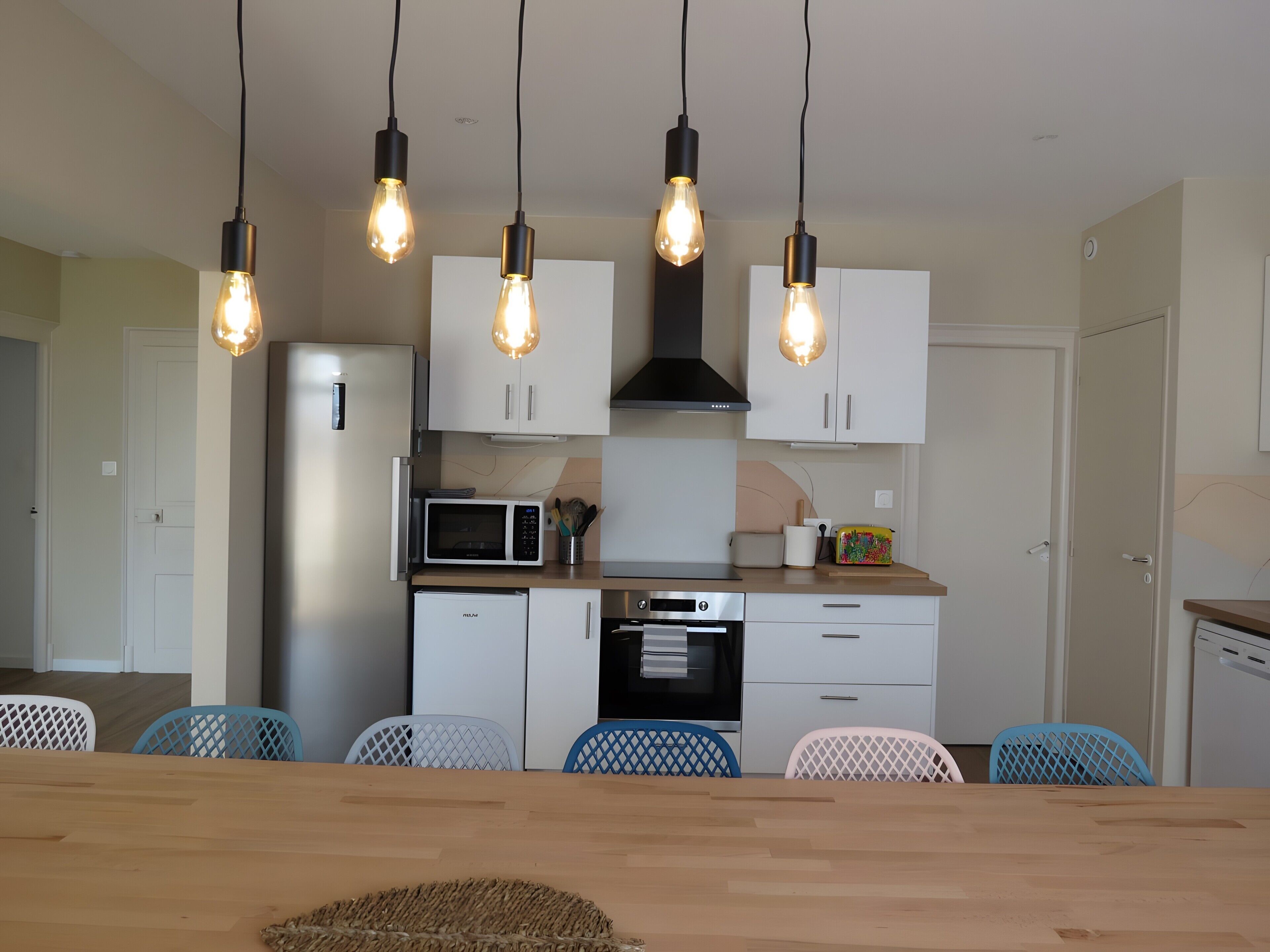 Une cuisine moderne avec des meubles blancs, un four à micro-ondes, un four traditionnel et une table à manger avec des chaises.