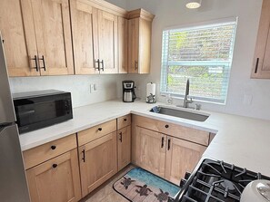 Eine Küche mit Holzschränken, einer Mikrowelle, einer Kaffeemaschine, einem Spülbecken und einem Fenster mit Jalousien.