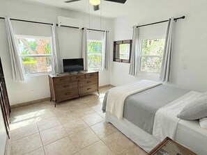 Ein Schlafzimmer mit einem Bett, einer Kommode und zwei fensterbepflanzten Fenstern.