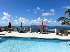 Ein Poolbereich mit Liegestühlen und Sonnenschirmen, freie Sicht auf das Meer und ein geflieste Poolufer.