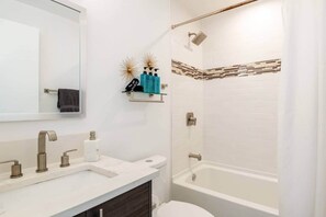 A modern bathroom with a large mirror, a sink with multiple faucets, a toilet, and a bathtub.