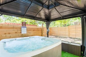 A hot tub under a covered area with a wooden fence and a safety sign.