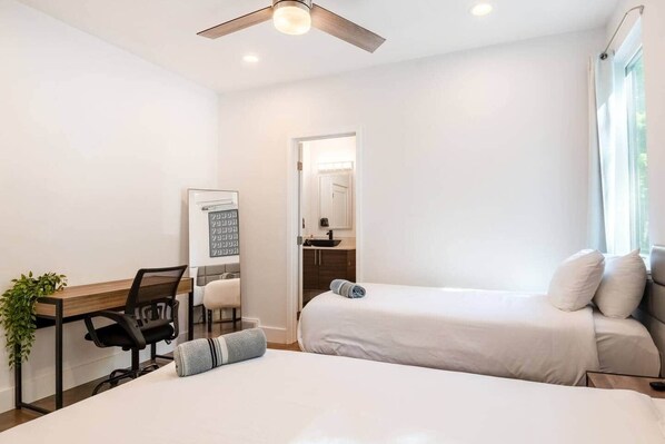 A hotel room with a bed, a desk, a chair, a small table, and a plant.