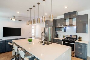Une cuisine moderne dotée d’un îlot central, d’appareils électroménagers en acier inoxydable et de luminaires suspendus.