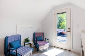 Una habitación con dos sillas, una mesita, una planta en maceta y un ventanal corredera que da a un espacio exterior.
