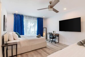 A hotel room with a bed, a desk, a chair, a TV, and a ceiling fan.