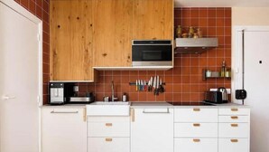 A kitchen with white cabinets, a wooden upper cabinet, a microwave, and a tiled backsplash. - Cocon cosy et lumineux · 1BDR · Bastille (Paris)