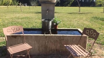 A concrete water feature with a stone basin and a metal bucket, surrounded by two metal chairs with flower designs.