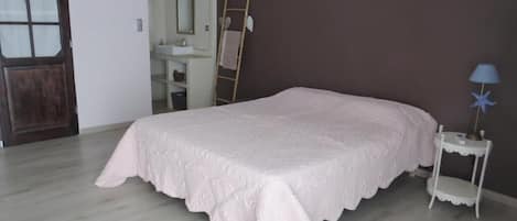 Quarto com cama, mesa de cabeceira pequena, espelho e porta.