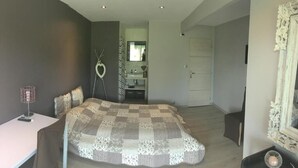 Ein Schlafzimmer mit einem großen Bett, einem Nachttisch, einem Sessel, einem Spiegel und einer Tür zu einem Badezimmer.
