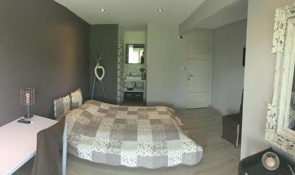 A bedroom with a large bed, a bedside table, a chair, a mirror, and a door leading to a bathroom. - Safranière des Sorgues (Le Thor)