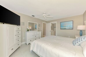 A bedroom with a bed, dresser, mirror, ceiling fan, and artwork on the wall. - Remodeled Siesta Key Villa – Steps to Private Beach & Village! (Sarasota)