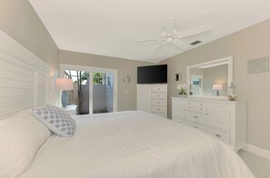 A bedroom with a bed, a ceiling fan, a TV, a dresser, and a door leading to an outdoor area. - Remodeled Siesta Key Villa – Steps to Private Beach & Village! (Sarasota)