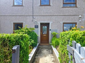 A building with a central entrance, a small garden area, and a paved pathway leading to the door. - Unique and character-filled cottage - Pass the Keys (Brynteg)