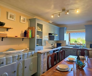 A kitchen with light blue cabinets, a wooden dining table, and a window with a view. - Unique and character-filled cottage - Pass the Keys (Brynteg)