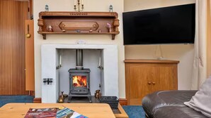 Ein Wohnzimmer mit Kamin, einem an der Wand befestigten Fernseher und einem Tisch mit Zeitschriften.
