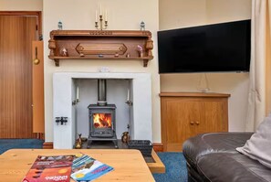 A living room with a fireplace, a television mounted on the wall, and a table with magazines. - Peaceful Property North of the island - Pass the Keys (Amlwch)