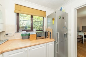 A compact kitchen with a microwave, toaster, and refrigerator, a window with a view of greenery, and a small dining area. - Quiet Green&Peaceful Home Near Reading University - Pass the Keys (Reading)