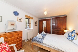Une chambre à coucher comprenant un lit, une armoire en bois, une commode et une fenêtre avec des stores.