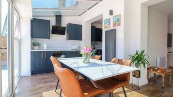Una cocina moderna con armarios oscuros, encimera de mármol y comedor con mesa y sillas.