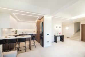 A modern kitchen with a central island, bar stools, and a built-in refrigerator. - Lumen Vitae Villa (Rethymno)