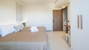 Quarto moderno com uma cama grande, uma mesinha de cabeceira, um guarda-roupa e uma porta que dá para outro cômodo.