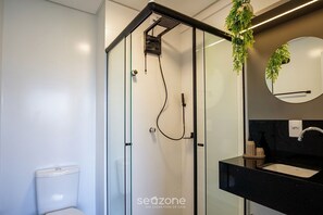 A modern bathroom with a glass-enclosed shower, a toilet, and a black countertop with a sink and mirror.