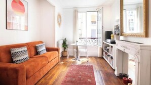A living room with a sofa, a small table, a fireplace, and a balcony with a view. - Cosy apartment in Sacré Cœur - 1BDR (Paris)