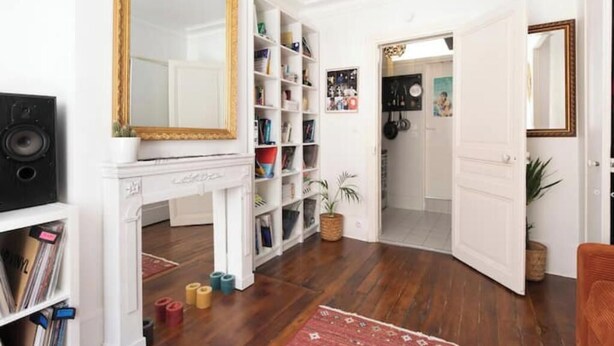 A room with a white fireplace, a large mirror, and a bookshelf. - Cosy apartment in Sacré Cœur - 1BDR (Paris)