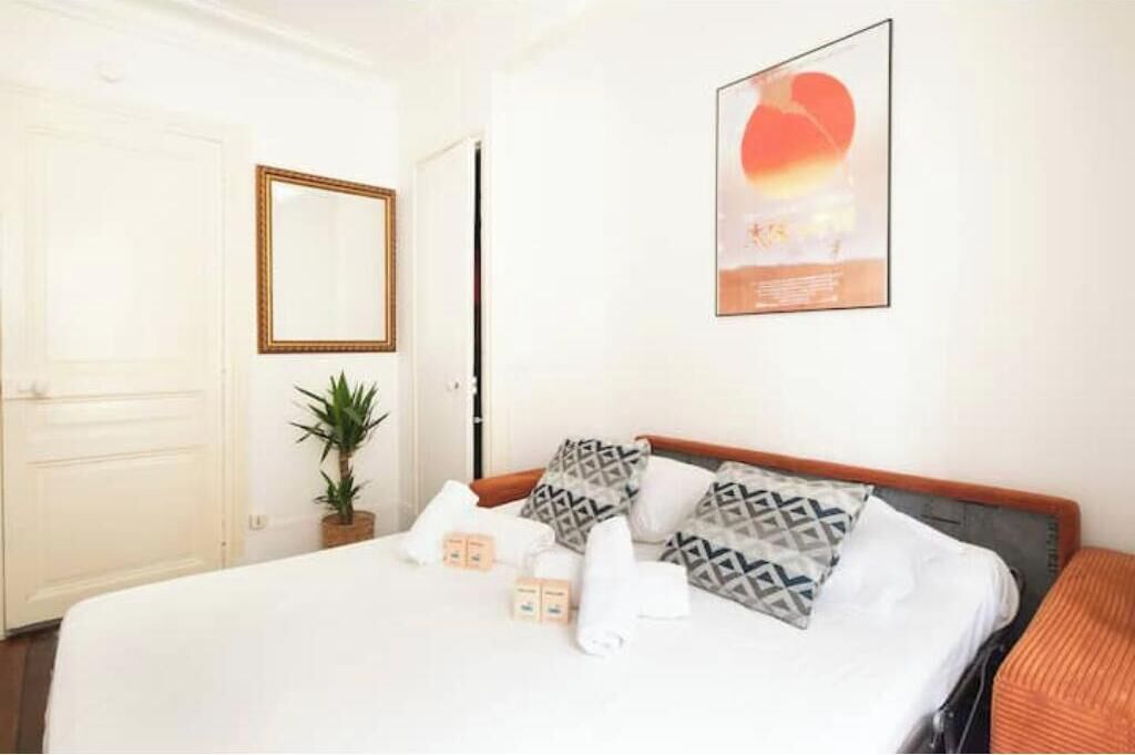 Hotelkamer met een bed, kussens, een kamerplant, een spiegel en een lijst met een afbeelding aan de muur.
