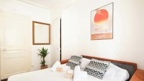 A hotel room with a bed, pillows, a potted plant, a mirror, and a framed picture on the wall. - Cosy apartment in Sacré Cœur - 1BDR (Paris)