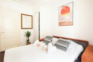 Ein Hotelzimmer mit Bett, Kissen, einem Blumentopf, einem Spiegel und einem gerahmten Bild an der Wand.