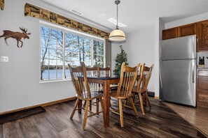 A kitchen with a dining table, chairs, a refrigerator, and a window overlooking a body of water. - Lake front Eagle River Chain of Lakes with indoor pool and jacuzzi! (Eagle River)