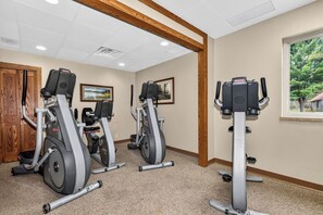 A gym with three elliptical machines, a wooden door, and a window with a view of trees. - Lake front Eagle River Chain of Lakes with indoor pool and jacuzzi! (Eagle River)
