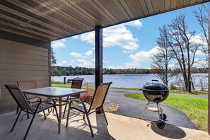 A covered patio with a table and chairs, a grill, and a view of a lake. - Lake front Eagle River Chain of Lakes with indoor pool and jacuzzi! (Eagle River)