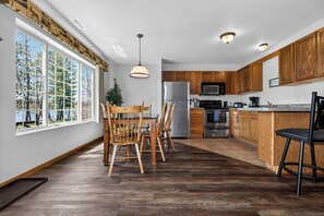A modern kitchen with wooden cabinets, stainless steel appliances, and a large window overlooking a forest. - Lake front Eagle River Chain of Lakes with indoor pool and jacuzzi! (Eagle River)