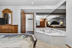 Ein Hotelzimmer mit einem großen Bett, einer Holzkommode, einem Badezimmer mit Badewanne und einem großen Spiegel, der den Raum widerspiegelt.