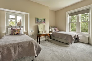 A bedroom with two beds, a nightstand, a chair, and a window with a view of trees.