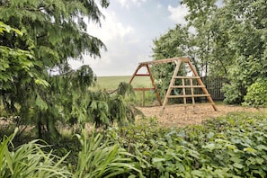 A wooden swing set in a garden with dense foliage and a clear sky.