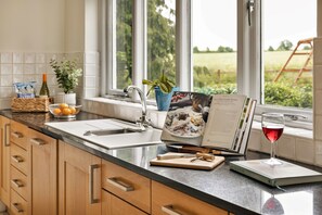 A kitchen with a window view, a sink, a wine glass, and a cookbook.