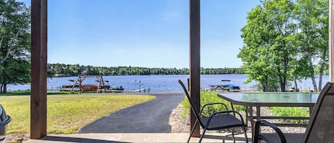 A covered outdoor area with a table and chairs, a swing set, and a view of a lake.