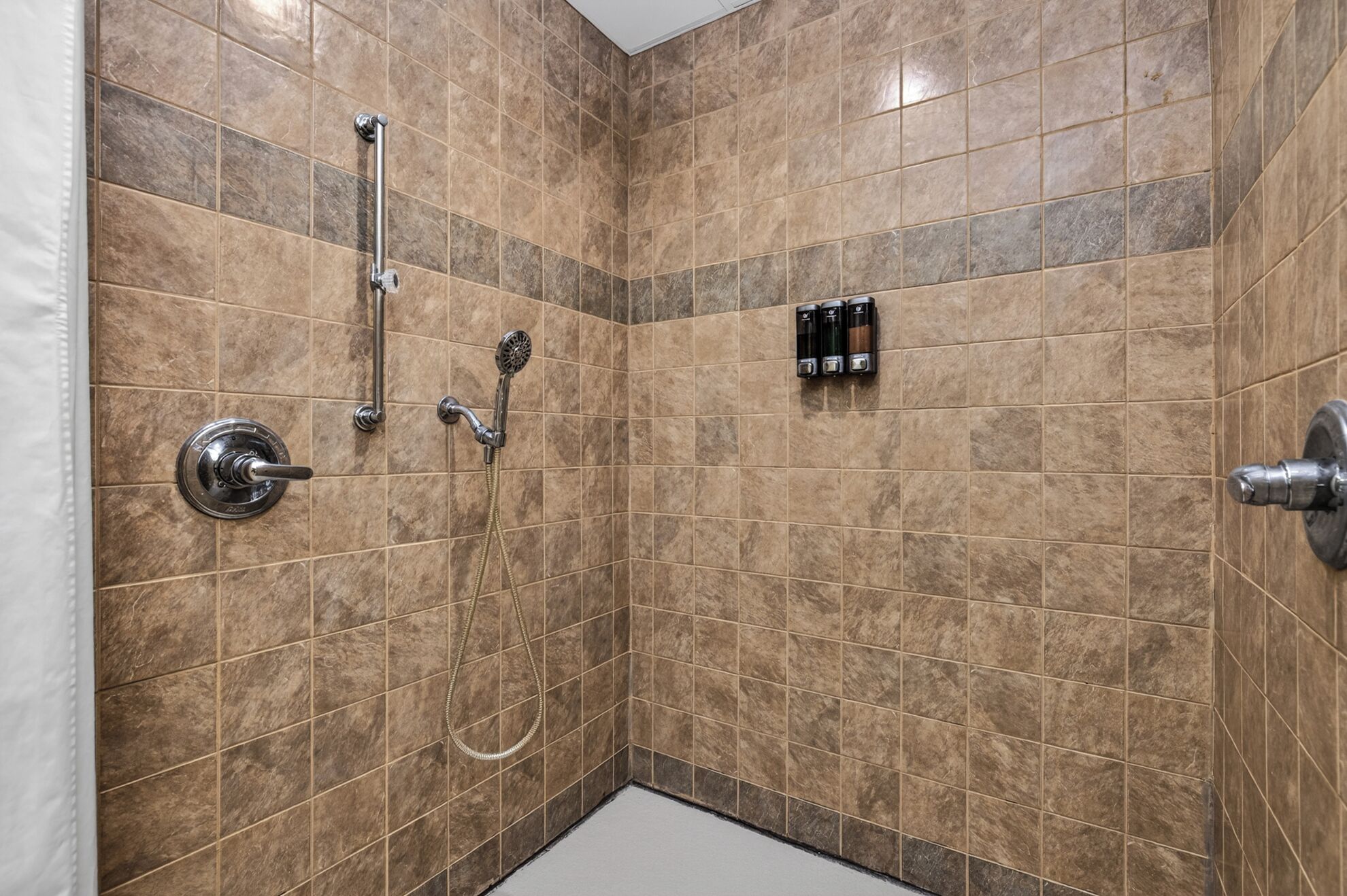 A shower with a handheld showerhead, a wall-mounted faucet, and a handheld showerhead.