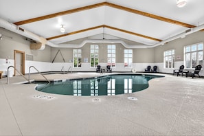 An indoor swimming pool with a high ceiling, wooden beams, and seating areas.