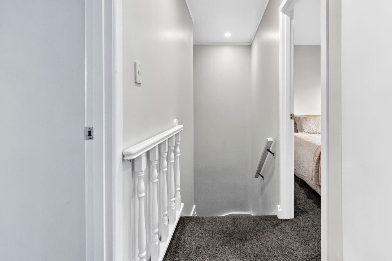 Un couloir étroit aux murs blancs, avec une porte blanche et un sol recouvert de moquette.