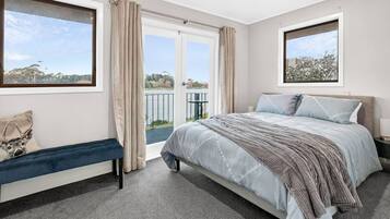 Quarto com cama, um banco, janela com vista e porta para uma varanda.